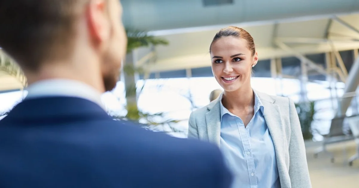 Professional Chauffeurz chauffeur greeting smiling female business traveller at London Luton Airport arrivals hall for private Luton airport transfer Meet and Greet service