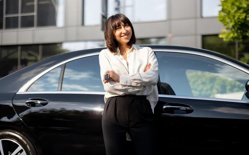 Private day journeys with Chauffeurz London Professional female chauffeur beside black Mercedes S-Class in London for private day journeys to Cotswolds and Stonehenge