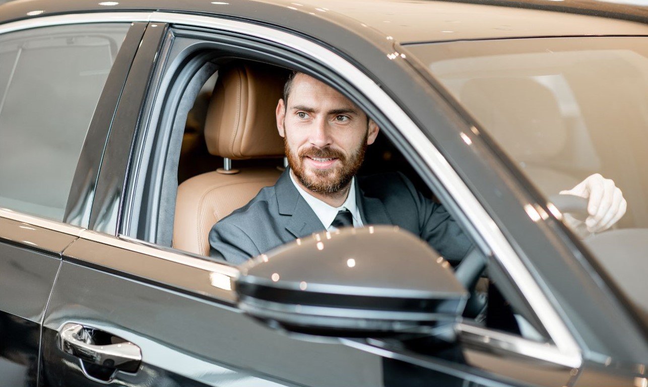 Professional chauffeur, smiling and helpful, driving a luxury car and waiting for the customer.