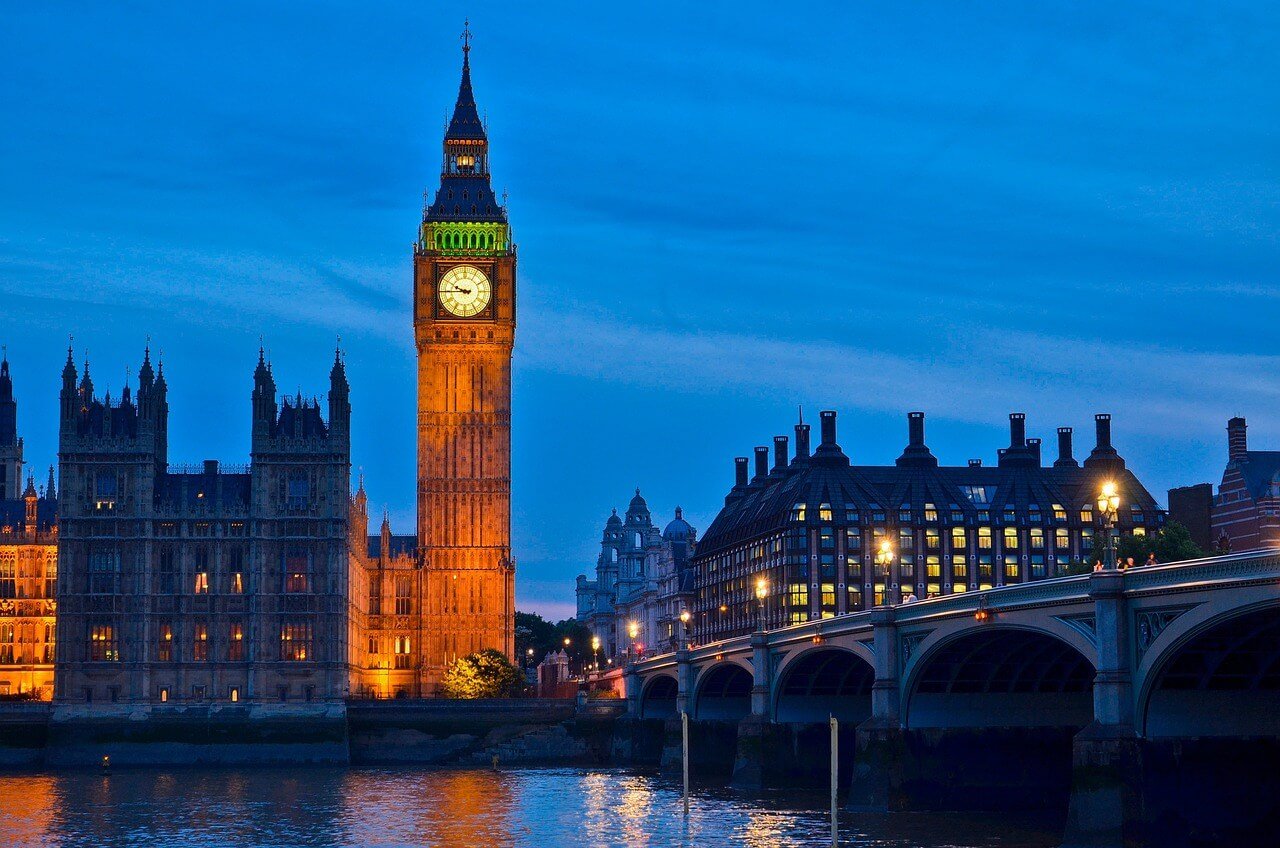 Big Ben and Westminster Palace illuminated at night, clock shining, with reflections in the River Thames, part of the London By Night Luxury Chauffeured Tour.