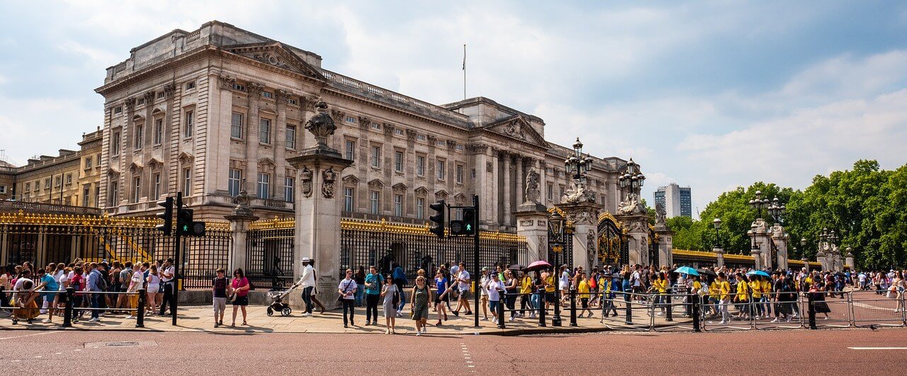 Buckingham Palace during the day, with crowds of tourists walking around the front square, a popular stop on the London sightseeing tour.