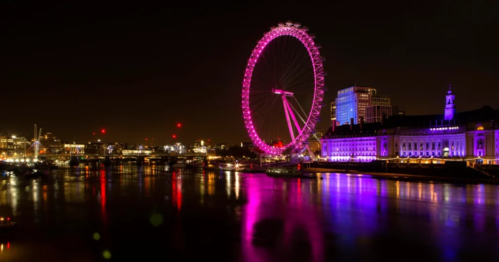 London Eye illuminated red at night with County Hall reflected in the Thames — London by Night private tour by chauffeur with Chauffeurz